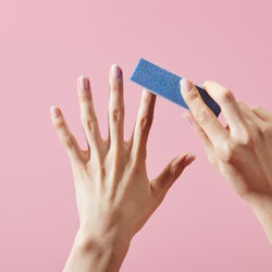 Limage manuelle des ongles naturels avec un polissoir à ongles bleu 4 faces sur fond rose